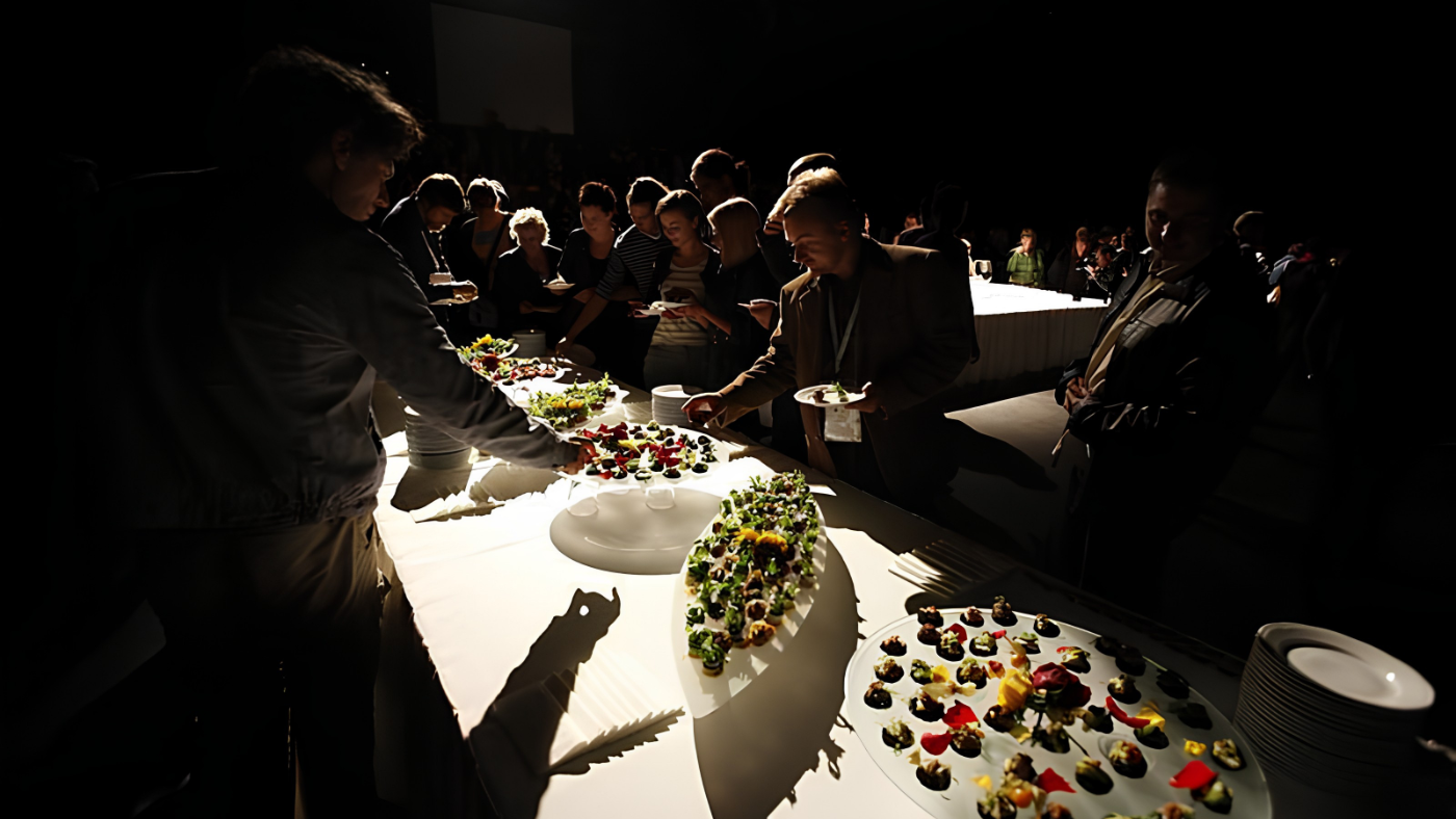 Audience members gathered in a dark performance space around a brightly lit table of edible sensory works at the European Congress of Culture.